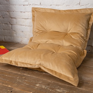 May include: A large, tan-colored, tufted floor cushion with a thick, plush fabric. The cushion is made of multiple layers of fabric, creating a comfortable and supportive seating option.