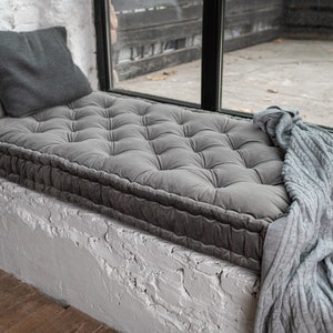 May include: A grey tufted window seat cushion with a grey knitted throw blanket draped over it.