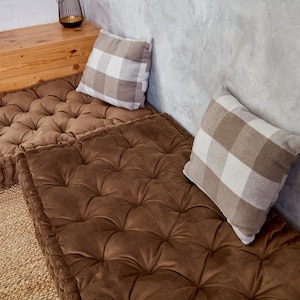 May include: Two brown floor cushions with tufted upholstery and a white and brown checkered pillow on each cushion.