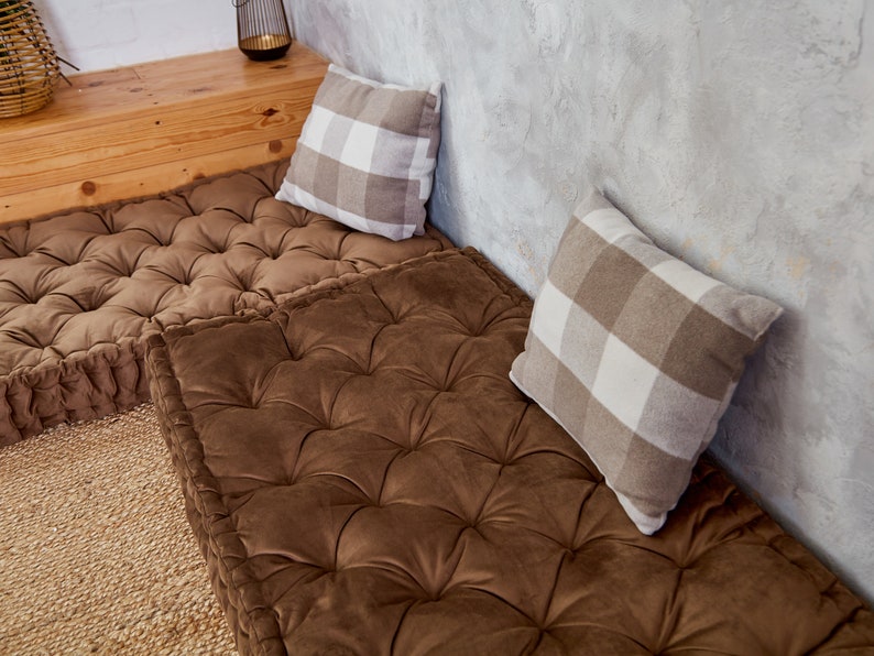 May include: Two brown floor cushions with tufted upholstery and a white and brown checkered pillow on each cushion.