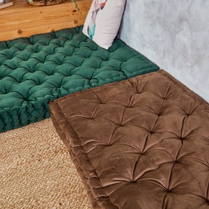 May include: Two square floor cushions, one green and one brown, with tufted button detailing. The cushions are made of a soft, plush fabric and are perfect for adding a touch of comfort and style to any room.