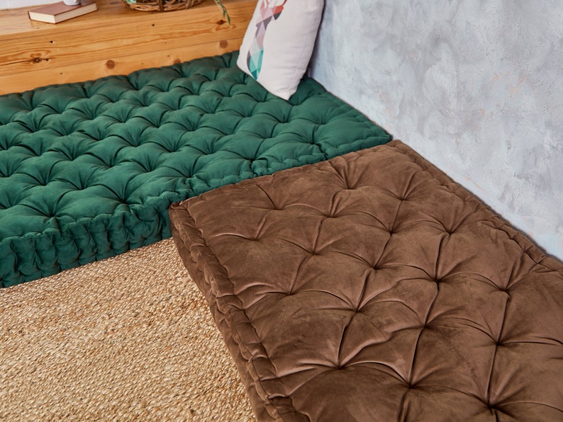 May include: Two square floor cushions, one green and one brown, with tufted button detailing. The cushions are made of a soft, plush fabric and are perfect for adding a touch of comfort and style to any room.