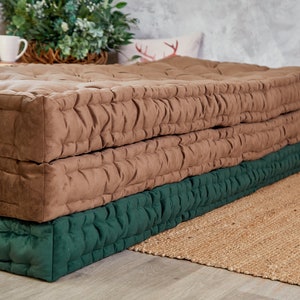 May include: A brown and green quilted floor cushion. The cushion is made of two layers, a top layer of brown fabric and a bottom layer of green fabric. The cushion is sitting on a woven rug.