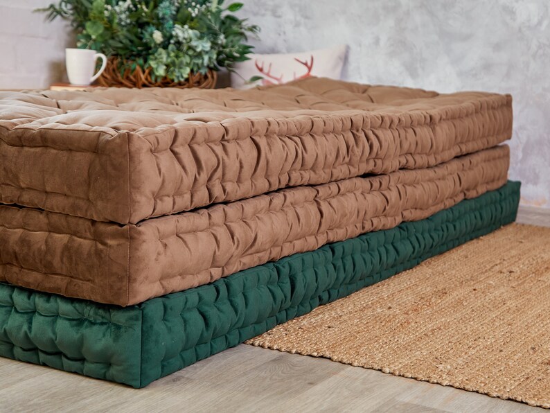 May include: A brown and green quilted floor cushion. The cushion is made of two layers, a top layer of brown fabric and a bottom layer of green fabric. The cushion is sitting on a woven rug.