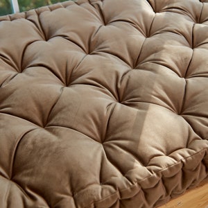 May include: A brown tufted cushion with a square shape and a stitched border. The cushion is made of a soft, velvety fabric.