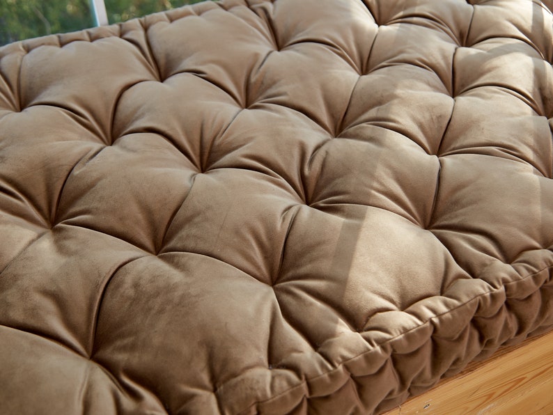 May include: A brown tufted cushion with a square shape and a stitched border. The cushion is made of a soft, velvety fabric.