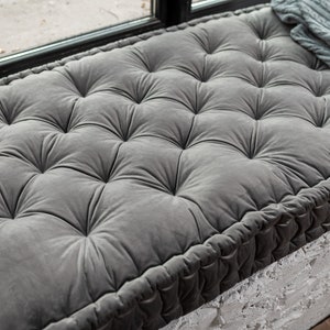 May include: A grey tufted floor cushion with a thick, rope-like border. The cushion is made of a soft, plush fabric and is perfect for adding comfort to any room.