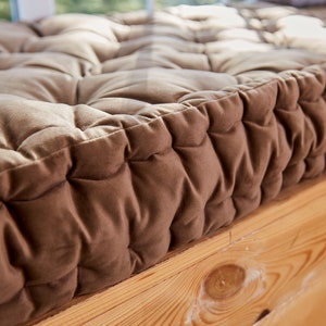 May include: Close-up of a brown tufted cushion with a thick, soft fabric. The cushion is placed on a wooden surface.