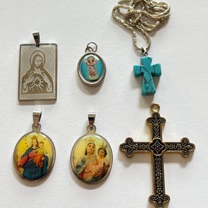 以下が含まれることがあります： 宗教的なイメージが描かれた銀と金のペンダント6個のセット。ペンダントには、イエスの描写がされた銀の四角いペンダント、聖母マリアと赤ちゃんのイエスの描写がされた銀の楕円形のペンダント、天使の描写がされた銀の楕円形のペンダント、ターコイズストーンが付いた銀の十字架のペンダント、そして複雑なディテールが施された金の十字架のペンダントが含まれています。