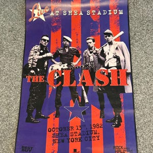 Puede incluir: Cartel del concierto de The Clash en el Shea Stadium, Nueva York, el 13 de octubre de 1982. El diseño presenta a los miembros de la banda, la palabra "The Clash" en letras grandes y los detalles del lugar sobre un fondo rojo y azul.