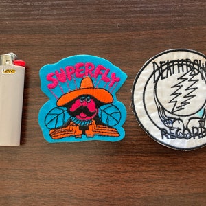 May include: Two embroidered patches. One is blue with a cartoon character wearing a sombrero and the text "Superfly". The other is white with black text that reads "Deathrow Records" and a lightning bolt design.