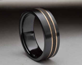 May include: A black ceramic ring with two thin gold bands.