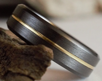 May include: A black and gold wedding band with a brushed finish. The band has a thin gold inlay.