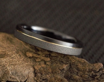 May include: A black and gold wedding band with a textured finish. The band is made of tungsten carbide and has a gold inlay.
