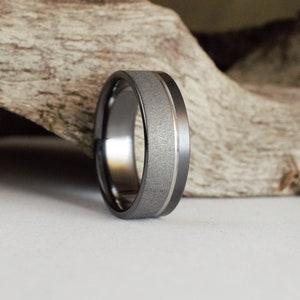 Puede incluir: Una banda de boda gris oscuro con una banda de plata cepillada en el centro.