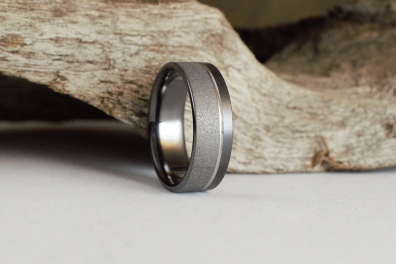 Puede incluir: Una banda de boda gris oscuro con una banda de plata cepillada en el centro.