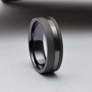May include: A black ceramic ring with a textured band and a polished black stripe.