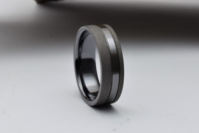 May include: A black ceramic ring with a textured band and a polished black stripe.