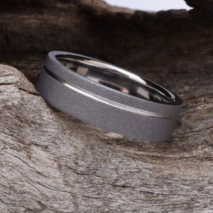 May include: A gray metal ring with a silver band around the center. The ring is textured and has a brushed finish.