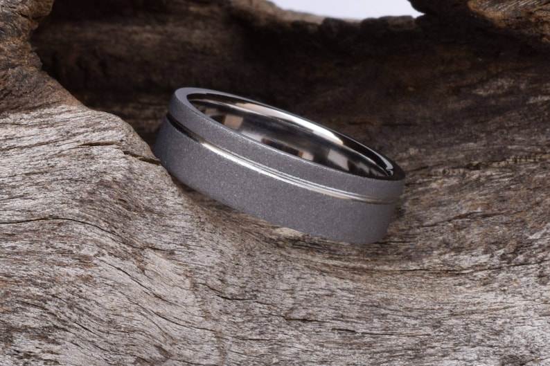 May include: A gray metal ring with a silver band around the center. The ring is textured and has a brushed finish.
