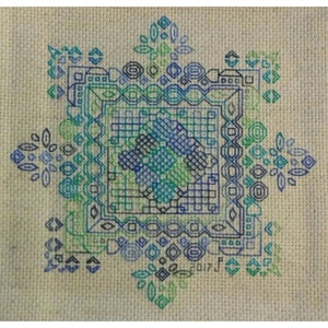 以下が含まれることがあります： 青、緑、黒の色合いの幾何学模様のクロスステッチパターン。パターンは、より小さな幾何学模様のボーダーで囲まれています。右下の隅に2017年が刺繍されています。