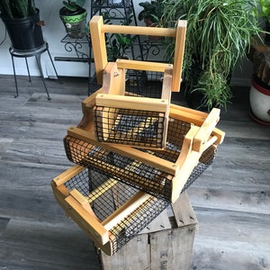 May include: Three wooden baskets with wire mesh bottoms are stacked on top of each other. The baskets are made of natural wood and have a rustic look. The baskets are perfect for storing and organizing items.