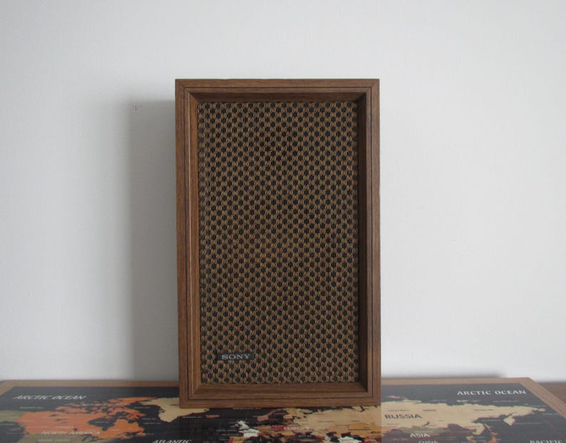 May include: A vintage Sony speaker with a brown wooden frame and a dark brown mesh speaker cover. The speaker has a rectangular shape and is designed for audio playback. The Sony logo is visible on the speaker.