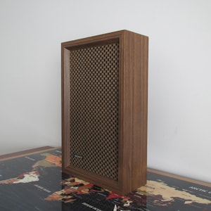 May include: A vintage wooden speaker with a brown mesh front. The speaker has a rectangular shape and a dark wood finish. The brand name "SONY" is visible on the speaker.
