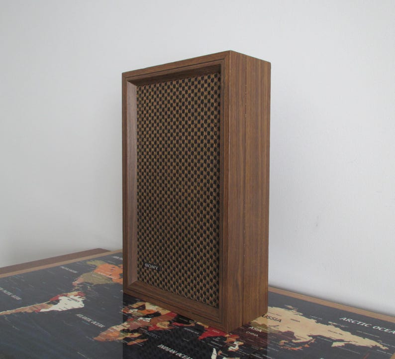 May include: A vintage wooden speaker with a brown mesh front. The speaker has a rectangular shape and a dark wood finish. The brand name "SONY" is visible on the speaker.