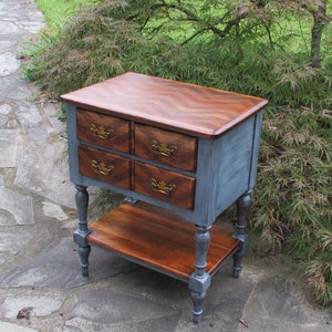 May include: A blue painted wooden end table with four drawers and a lower shelf. The top of the table has a herringbone pattern in a darker wood.