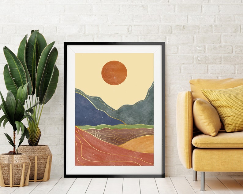 May include: A framed abstract landscape print with a large orange sun, blue and green mountains, and gold lines on a beige background.