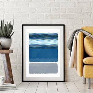 May include: A framed abstract print with a white background and three horizontal stripes in shades of blue and gray. The top stripe is a series of thin, white lines with blue spaces between them. The middle stripe is a solid blue color. The bottom stripe is a solid gray color.
