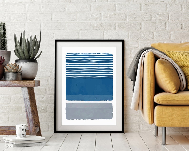 May include: A framed abstract print with a white background and three horizontal stripes in shades of blue and gray. The top stripe is a series of thin, white lines with blue spaces between them. The middle stripe is a solid blue color. The bottom stripe is a solid gray color.