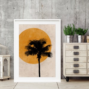K&ouml;nnte beinhalten: Gerahmter Kunstdruck mit einer schwarzen Palmensilhouette vor einer gelben Sonne auf beigem Hintergrund. Das Kunstwerk ist in einem wei&szlig;en Rahmen, der ein tropisches Thema suggeriert. Das Bild wird vor einer neutralen grauen Wand pr&auml;sentiert.