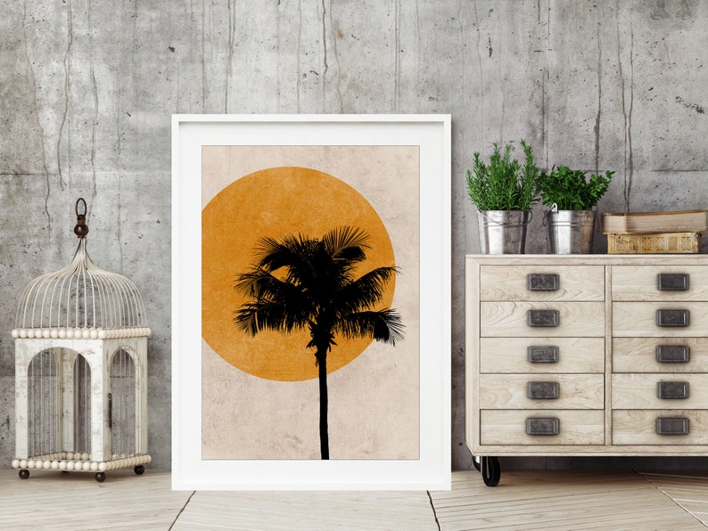 K&ouml;nnte beinhalten: Gerahmter Kunstdruck mit einer schwarzen Palmensilhouette vor einer gelben Sonne auf beigem Hintergrund. Das Kunstwerk ist in einem wei&szlig;en Rahmen, der ein tropisches Thema suggeriert. Das Bild wird vor einer neutralen grauen Wand pr&auml;sentiert.