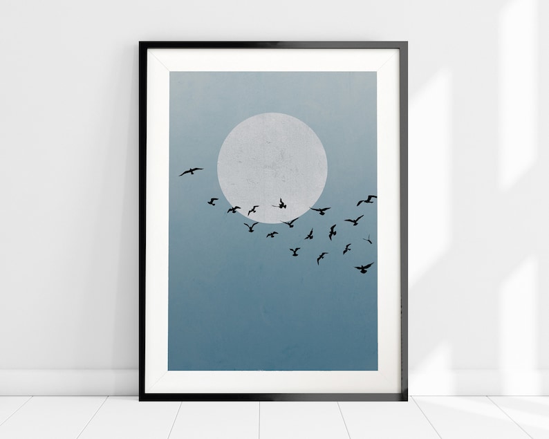 Op de afbeelding: Een ingelijste print van een minimalistische illustratie van een zwerm vogels die vliegt voor een grote, witte maan tegen een blauwe lucht.