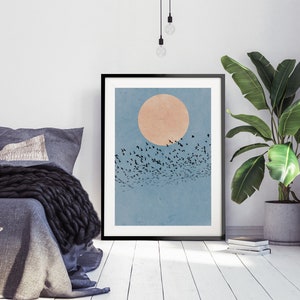 Pu&ograve; includere: Una stampa incorniciata di un'illustrazione minimalista di uno stormo di uccelli che vola davanti a un grande sole arancione pallido su uno sfondo di cielo blu.