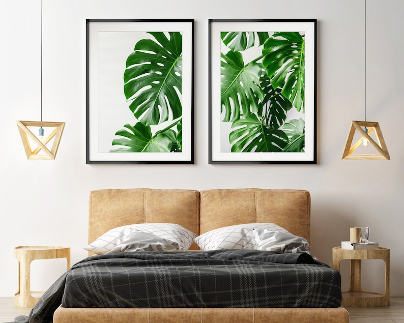 May include: Two framed prints of green monstera leaves against a white background, hanging above a brown leather headboard with a black and white plaid bedspread.