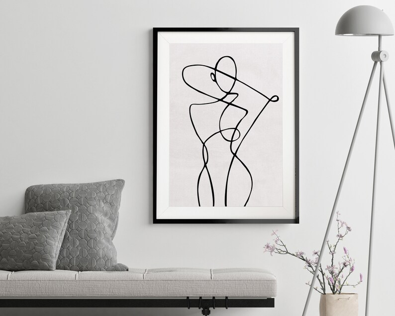 K&ouml;nnte beinhalten: Schwarz-wei&szlig;-Linienkunst-Druck einer stilisierten Figur im minimalistischen Stil. Der Druck ist in einem schwarzen Rahmen gerahmt und h&auml;ngt an einer wei&szlig;en Wand.