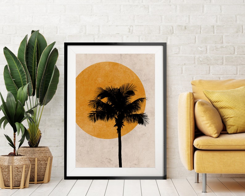 K&ouml;nnte beinhalten: Schwarz gerahmter Kunstdruck mit einer Palmensilhouette vor einer gro&szlig;en orangefarbenen Sonne. Das Kunstwerk wird in einem modernen Wohnzimmer mit einem gelben Sofa und Topfpflanzen pr&auml;sentiert. Der Kunstdruck verleiht eine tropische Note.
