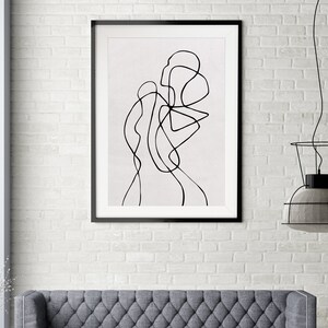 May include: Black and white line art print of an abstract figure in a frame. The print is on a white background and is hanging on a white brick wall.