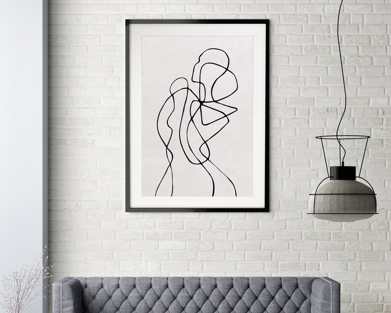 May include: Black and white line art print of an abstract figure in a frame. The print is on a white background and is hanging on a white brick wall.