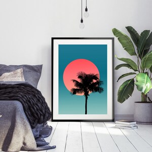 Pode incluir: Uma impress&atilde;o emoldurada de uma silhueta de palmeira contra um p&ocirc;r do sol rosa e azul. A impress&atilde;o est&aacute; em uma moldura preta e est&aacute; pendurada em uma parede branca.