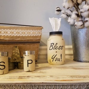 K&ouml;nnte beinhalten: Ein wei&szlig; bemaltes Einmachglas mit einem schwarzen Deckel und den Worten "Bless You!" darauf. Das Glas ist mit Taschent&uuml;chern gef&uuml;llt und dient als Taschentuchspender. Es gibt zwei kleine wei&szlig;e bemalte Gl&auml;ser mit schwarzen Deckeln und den Buchstaben "S" und "P" darauf. Die Gl&auml;ser stehen auf einer wei&szlig;en Holzoberfl&auml;che.