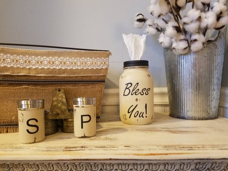 K&ouml;nnte beinhalten: Ein wei&szlig; bemaltes Einmachglas mit einem schwarzen Deckel und den Worten "Bless You!" darauf. Das Glas ist mit Taschent&uuml;chern gef&uuml;llt und dient als Taschentuchspender. Es gibt zwei kleine wei&szlig;e bemalte Gl&auml;ser mit schwarzen Deckeln und den Buchstaben "S" und "P" darauf. Die Gl&auml;ser stehen auf einer wei&szlig;en Holzoberfl&auml;che.