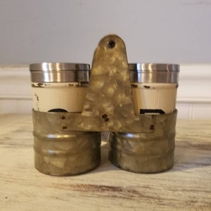 K&ouml;nnte beinhalten: Ein Set aus zwei Salz- und Pfefferstreuern aus Metall mit einer patinierten, verzinkten Oberfl&auml;che. Die Streuer werden von einem Metallgestell mit Griff zusammengehalten.