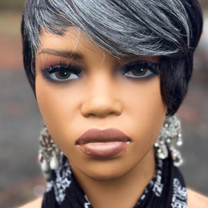 May include: A woman with short, black hair with streaks of gray. She is wearing a black and white bandana and has a neutral expression on her face.