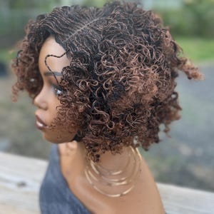 May include: A short, curly wig with a blend of dark brown and auburn tones. The wig features a natural-looking hairline and is styled in a voluminous, textured bob. The model is wearing gold hoop earrings and a gray top.