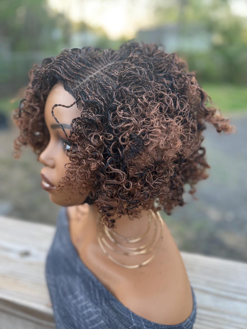 May include: A short, curly wig with a blend of dark brown and auburn tones. The wig features a natural-looking hairline and is styled in a voluminous, textured bob. The model is wearing gold hoop earrings and a gray top.