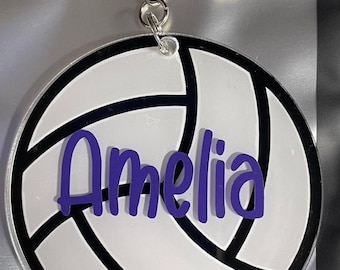 Puede incluir: Llavero de voleibol blanco con contorno negro y el nombre Amelia escrito en morado.
